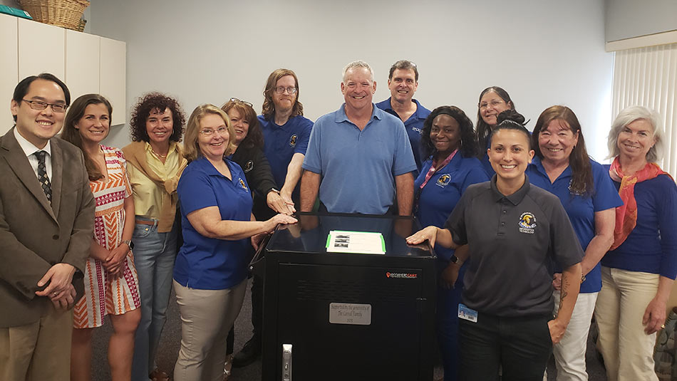 group shot of Carroll family and students, advisors, deans and professors standing behind a cart full of laptops