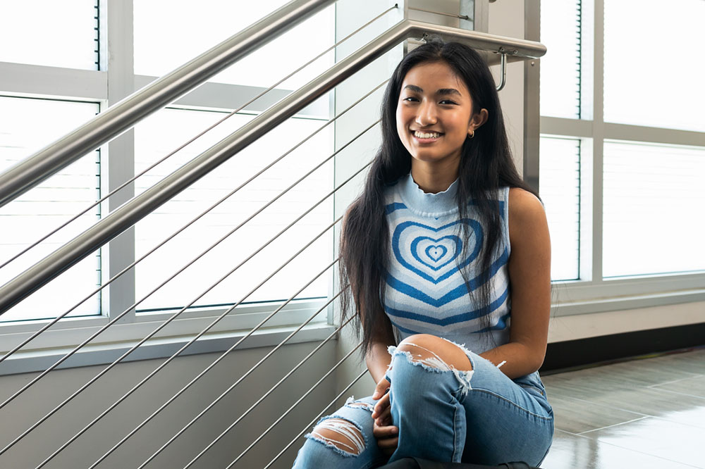 female SPC  student wearing a sleeveless shirt and blue jeans sitting on stairs