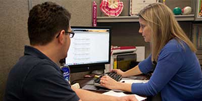 two people seated at a desk looking at a laptop