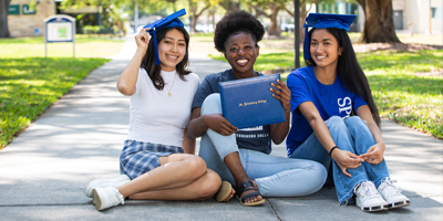 3 female SPC students seated on a walkway showing off diploma