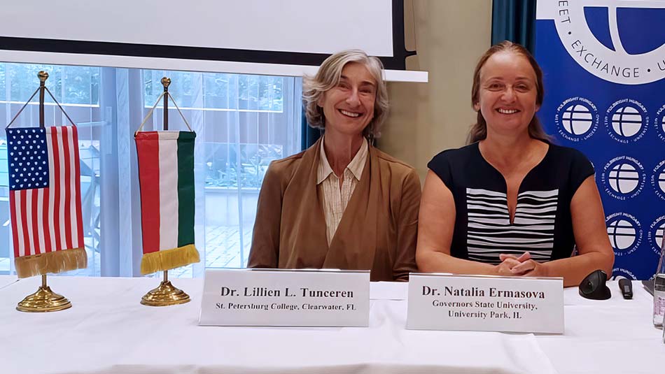 Doctors Tunceren and Ermasova seated at a table behind their nameplates and beside the USA and Hungary flags.