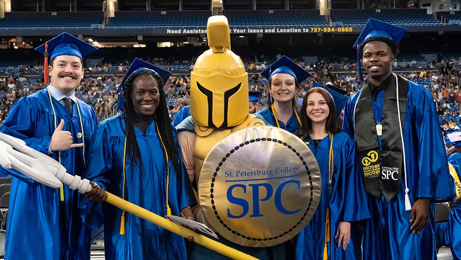 five SPC graduates in graduation robes standing with Titus, the school mascot