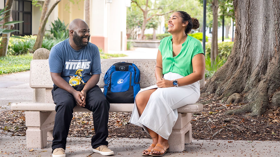 male student in a blue titans tshirt laughing with another SPC student in a green shirt outside on the Clearwater Campus