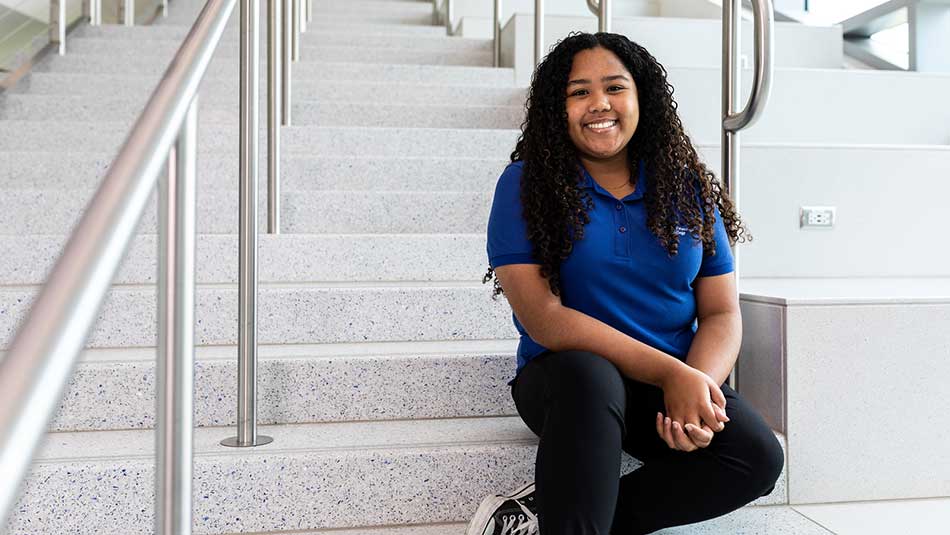 female SPC student wearing a blue polo shirt sitting on the stairs at the Gibbs Campus