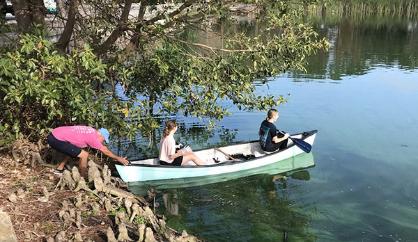 students in a canoe cleaning up a pond