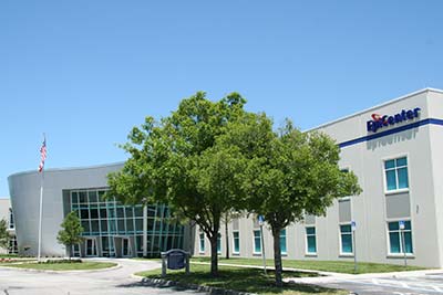 The modern-looking SPC EpiCenter building behind tall, green trees and under a blue sky.