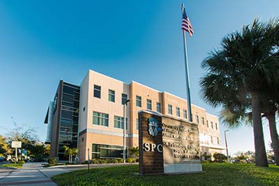 The SPC Epi-Services building pictured behind tall oak trees, with the blue SPC sign in the foreground.