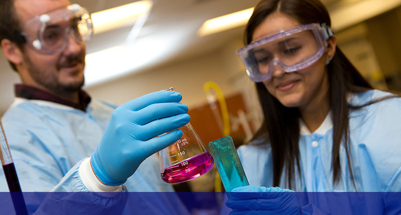 male student holding a beaker while female student takes measurements both wearing blue gloves