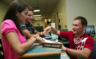 2 students speaking to an assistant at his desk