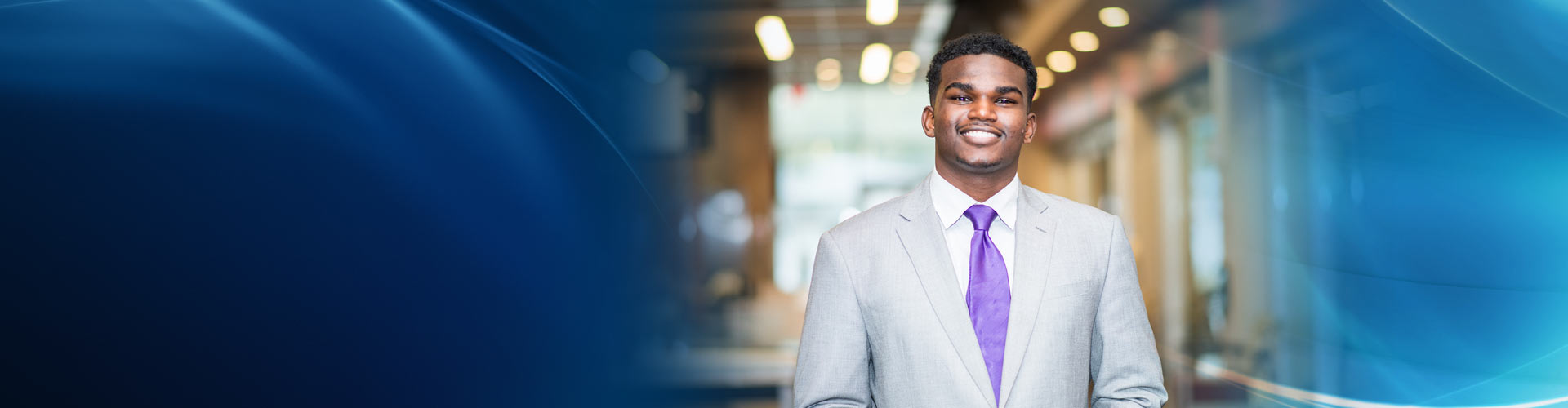 A male students smiling in a white business suit on a blue gradient background