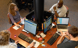 a group of students talking while sitting with laptops