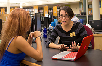 2 women speaking while seated at a table with a laptop